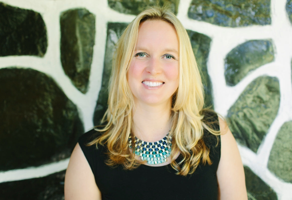Kate Love of Seeking Ceremony smiles at the camera in front of a black stone wall