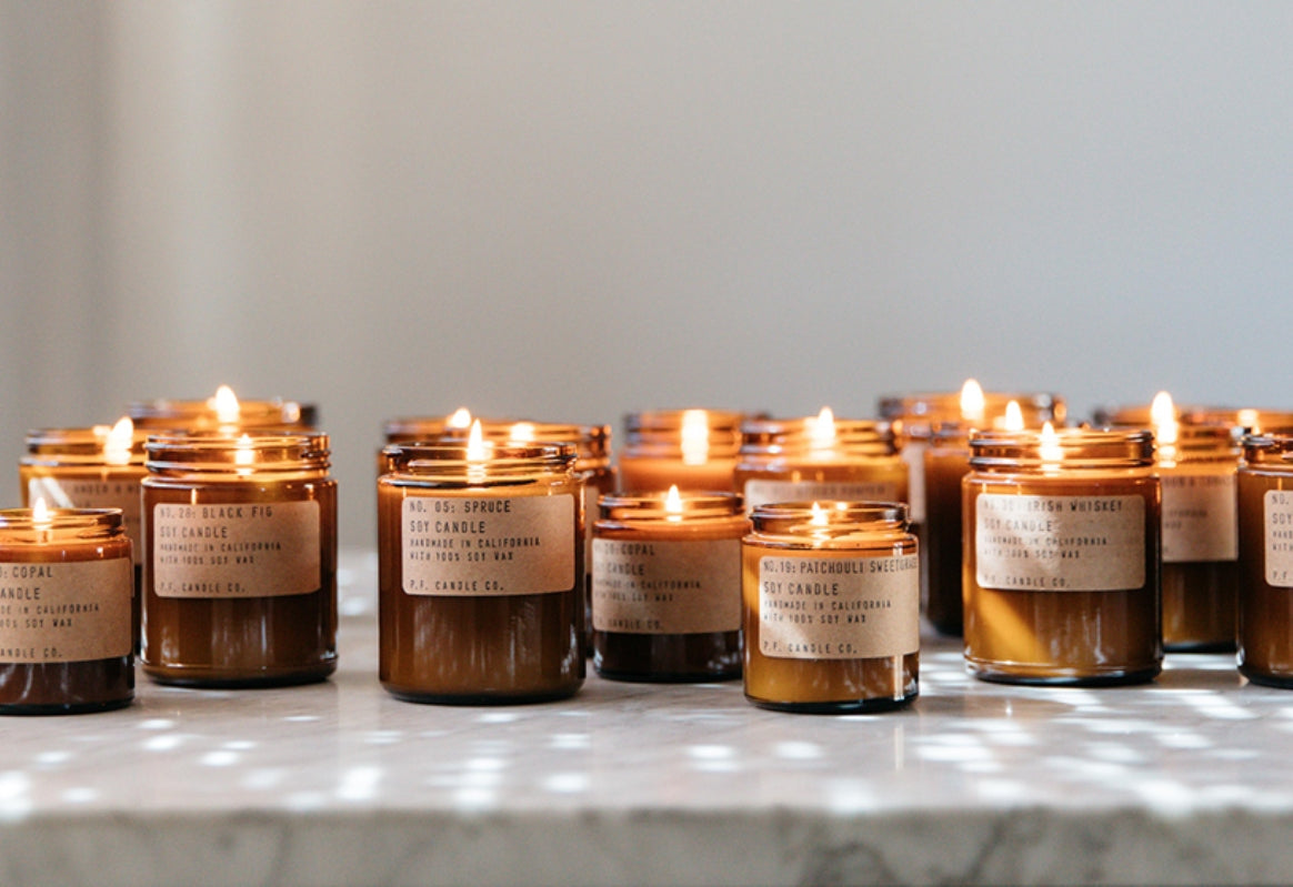 Rows of amber glass soy candles with simple kraft labels offer a warm light, resting on a marble countertop